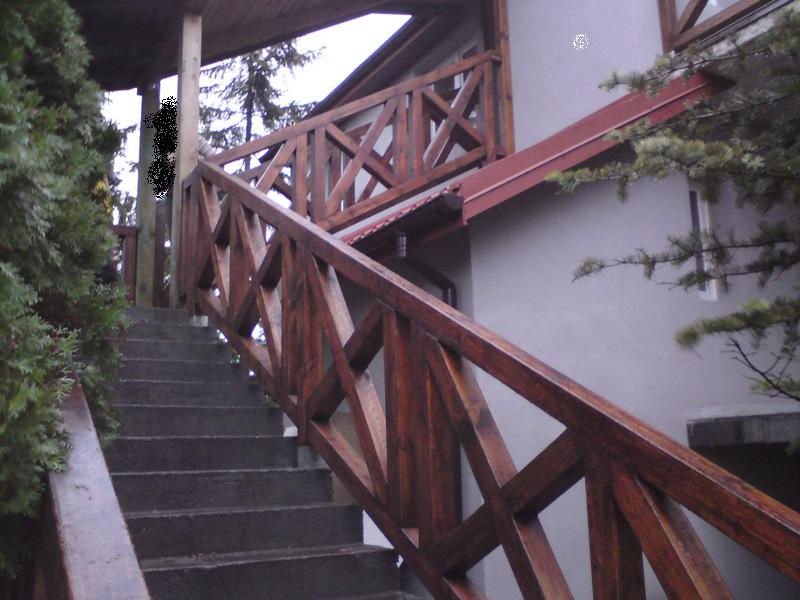 Zewnętrzne betonowe schody z drewnianą balustradą o krzyżowym wzorze, prowadzące do wejścia budynku.